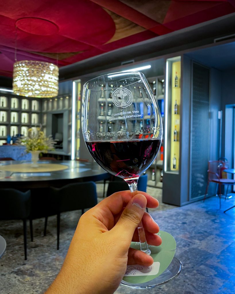 Tempio_Brunello_vino bicchiere di vino rosso tenuto in mano all'interno di una delle sale del tempio del brunello a montalcino